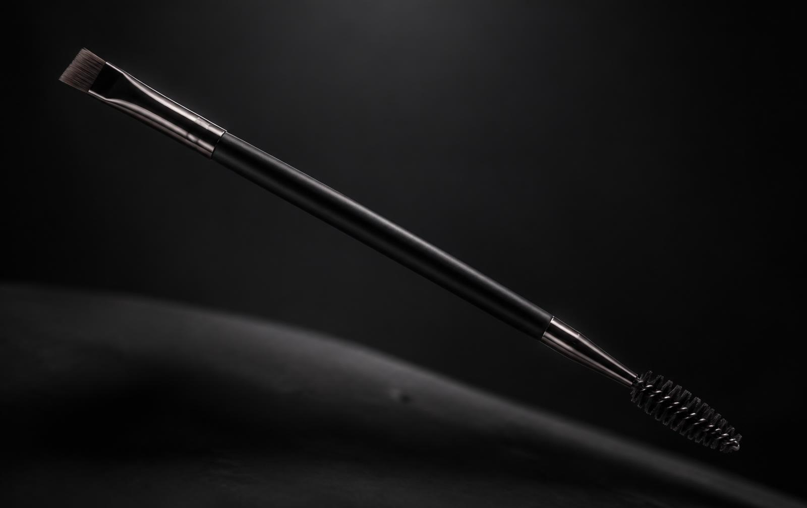 AMY brow brush lit dramatically against a near-black background